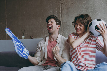 Exultant couple friends woman man football fans 20s in casual clothes foam glove finger up support...