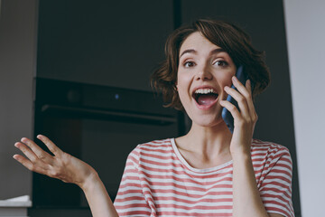 Young surprised amazed housewife woman 20s in casual clothes striped t-shirt talking by mobile cell...