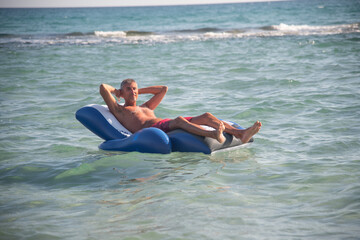 Fototapeta na wymiar Man relaxing on a water inflatable chair in the sea. Holiday concept