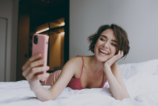 Full body blogger young woman in pajamas lying in bed do selfie shot mobile cell phone camera post on social network rest relax on weekends indoors at home. Good mood night morning bedtime concept