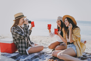 Full body three friends fun young women in straw hat summer clothes have picnic hang out take photo drink liguor glasses raise toasts outdoors on sea beach background People vacation journey concept.