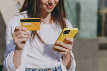 Cropped up photo oung woman in shirt stand in front city building walk in town centre use mobile cell phone credit bank card shopping online order delivery book tour outdoors Urban lifestyle concept.