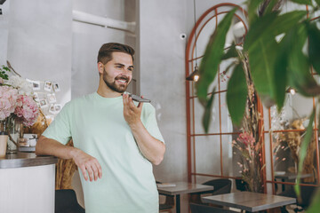 Bottom view young man in mint t-shirt buy takeaway paper cup coffee record voice message on mobile...