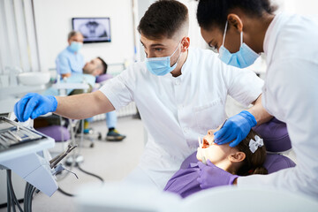 Small girl getting her teeth checked by two dentists at dental clinic.