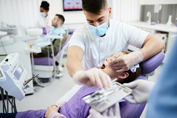 Male dentist examining little girl's teeth during dental appointment at dentist's office.
