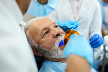 Senior man having dental procedure with dental curing UV light at dentist's office.