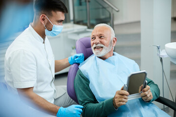 Satisfied senior man communicating with dentist after dental procedure at dentist's office.