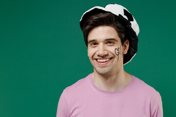 Young happy smiling man fan wear basic pink t-shirt hat go text on cheek cheer up support football sport team watch tv live stream scream look camera isolated on dark green color background studio