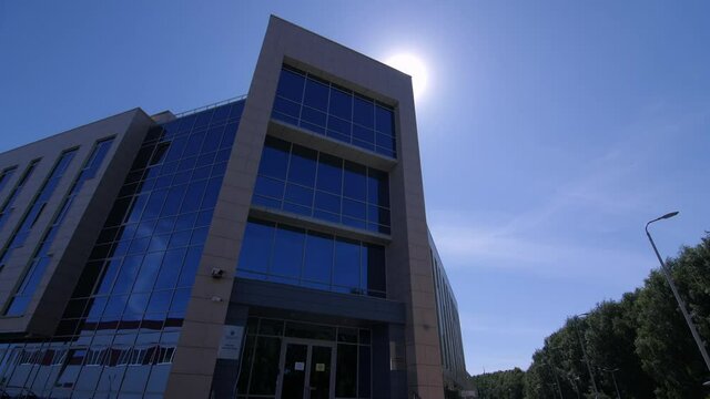 Elegant office building with glass facade and stylish entrance on city street under blue sky on sunny spring day