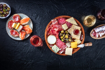Charcuterie and cheese board, overhead flat lay composition with copy space on a black background. Italian antipasti or Spanish tapas, shot from above with wine, olives, and sanwiches