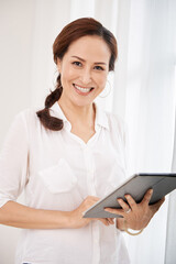 Portrait of happy excited elderly businesswoman in white shirt holding digital tablet in hands looking at camera