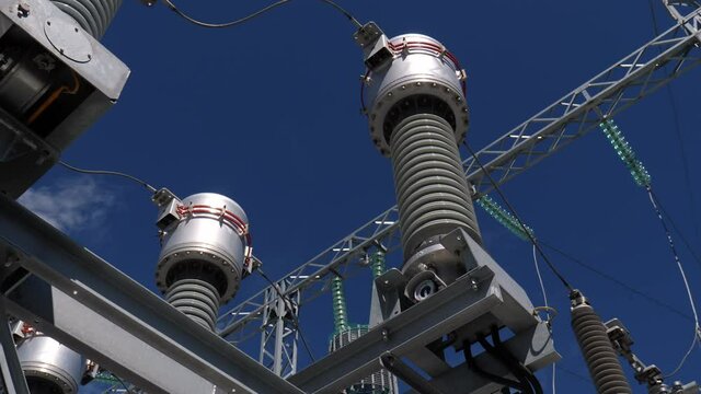 Insulators with cables on supports on electricity production substation switchyard under blue sky close low angle shot