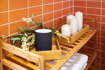A closeup shot of a cup, a branch of a plant, and candles in the bathroom