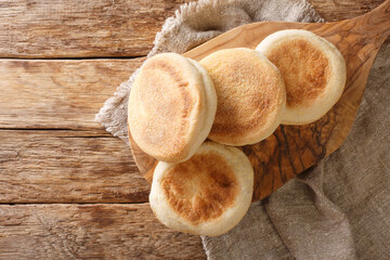 For a delicious breakfast, English muffins buns close-up on a wooden board on the table. horizontal top view from above
