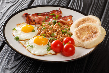 Delicious breakfast or lunch with fried eggs, beans, bacon, tomatoes and English muffins close-up in a plate on the table. horizontal