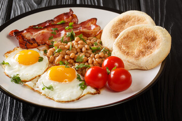 Fototapeta na wymiar Fried eggs, beans, bacon, tomatoes and English muffins close-up in a plate on the table. horizontal