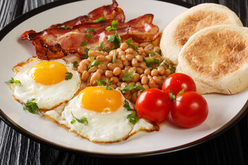Classic breakfast serving of fried eggs, beans, bacon, tomatoes and muffins close-up in a plate on the table. horizontal