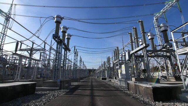 Motion across electricity distribution substation switchyard with different equipment under clear blue sky on sunny day