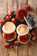 English muffins with strawberry jam close-up on the table, rustic style. Vertical top view from above