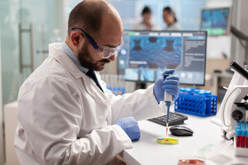 Scientist dropping blood sample with micropipette on petri dish in genetic laboratory. Team of...