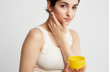 Obraz na płótnie Canvas brunette in a white tank top yellow cream jar skin care