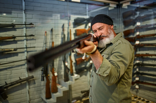 Bearded hunter choosing hunting rifle in gun store