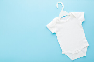 White new baby bodysuit on hanger on light blue table background. Pastel color. Closeup. Empty...