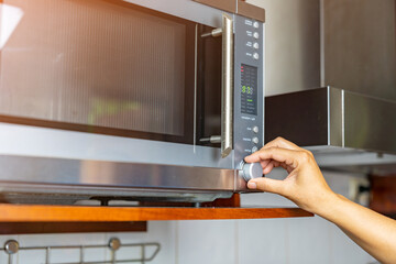 Woman setting timer for cooking food in microwave.