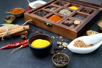 Variety of Indian spices and herbs in a wooden box. Multicolored spices in a wooden organizer, top view. Seasoning background. Bay Leaf, Black Pepper, Cinnamon, Cloves, Coriander, Turmeric, red chili.