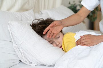 Caring mom check small sick boy temperature with hand. Ill kid with flu or covid illness sleep in...