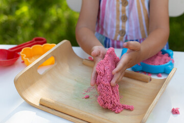Hands of little girl playing with kinetic sand close-up. Leisure activity outdoors in summer day.