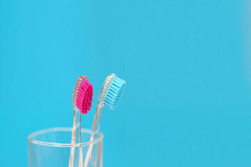 Two colored toothbrushes in a glass on a blue background. Blue and pink toothbrushes. Close-up. Space for text