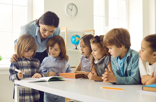 Little school children learning to write. Happy kids acquiring new skills in class. Young school teacher helping her cute little students who are writing in their notebooks or activity books