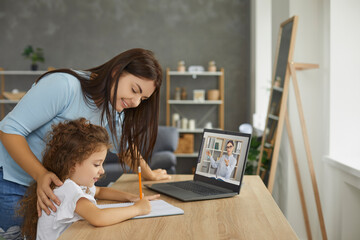 Mum and little child learning at home, sitting at table, watching web tutorial for kids on screen of laptop computer, having online class with school teacher, doing homework with help of private tutor