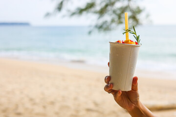 Close up fruit juice in plastic disposable cup on defocused beach background