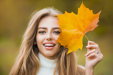 Happy autumn woman having fun with leaves outdoor in park. Close up portrait photo of young girl on blurred park fall background, leaves falling.