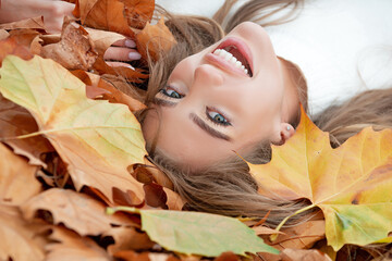 Young beautiful girl lying on yellow leaves in the autumn park.
