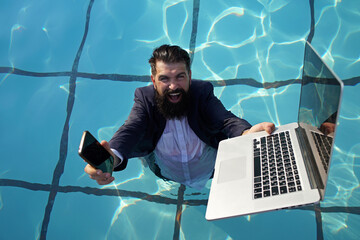 Funny bearded business man in suit using phone and laptop in swimming pool. Concept of young people...