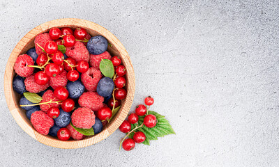 fresh berries of raspberries, red currants and blueberries in a plate on a light concrete background