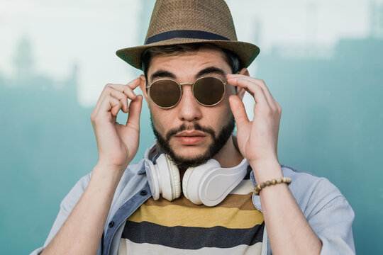 Young hipster man looking at camera outdoor wearing headphones during summer travel vacations - Focus on face