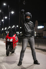 A motorbiker stands among the night street with a raised up fist.