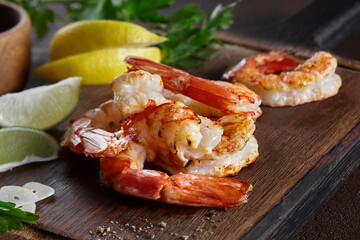Grilled prawn tails with lemon, lime, garlic and greens on wooden board