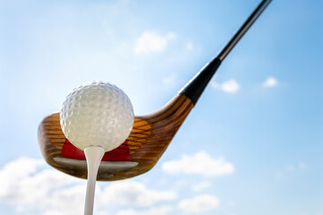 Golf club and golf ball about to tee off against a blue sky