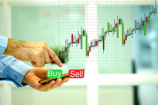 A man holding a smartphone and press sell or buy button in the virtual stock market. The financial chart or candlestick chart to buy and sell for stock exchange market concept. - Powered by Adobe