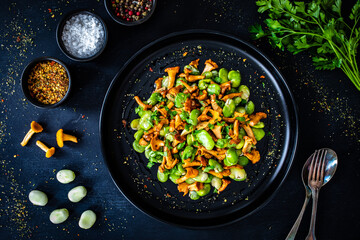 Broad beans salad with fried chanterelles, garlic and parsley on wooden table
