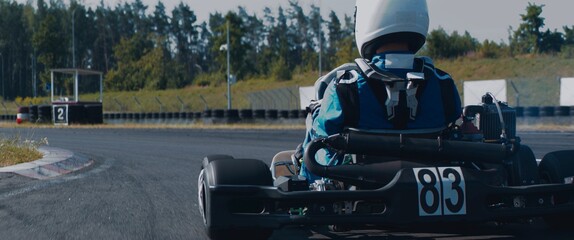 Back view of teenager professional racer driving his go kart on a race track