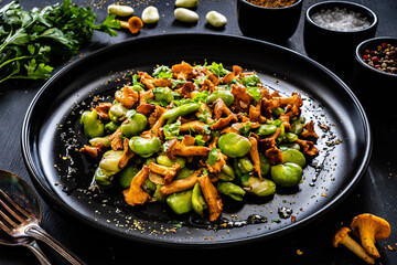 Broad beans salad with fried chanterelles, garlic and parsley on wooden table

