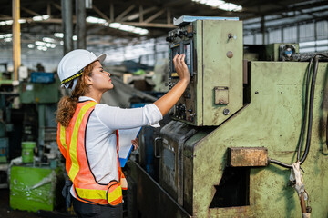 Fototapeta na wymiar Female African American worker wearing uniforms safety and hardhat are checking system machines in the factory. woman in large industrial factory.