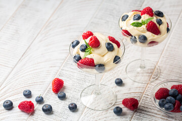 Italian mascarpone cream with berries - Crema di mascarpone e frutti di bosco. White wood table. Text space.