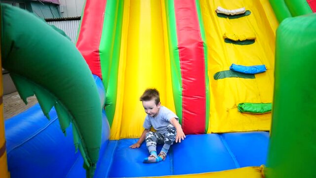 A little boy slides down a slide on a colorful trampoline platform